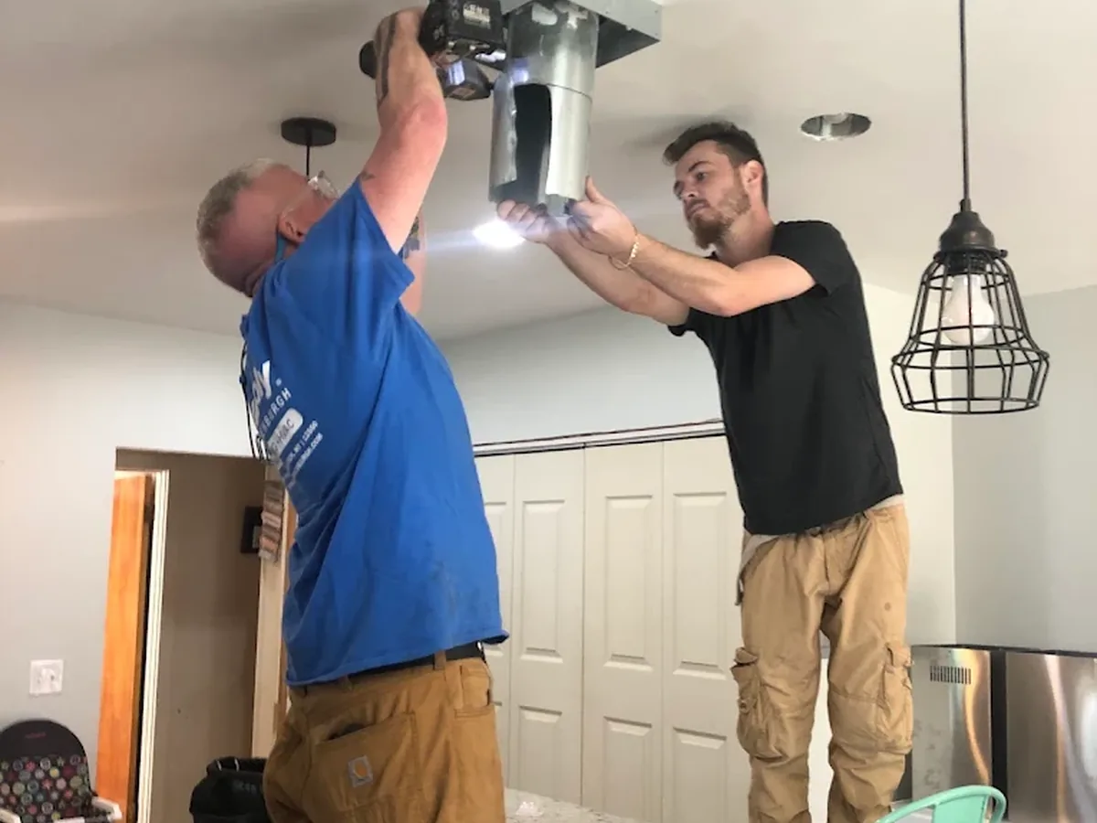 Two Uppercut Plumbing technicians installing a ceiling vent in a customer's kitchen