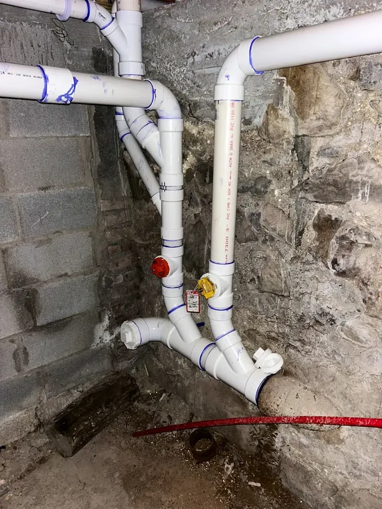 New PVC drain and vent stacks run against a stone foundation wall
